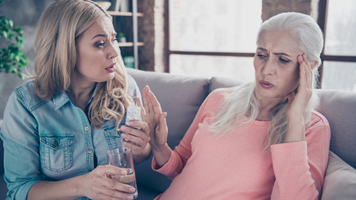 Jonge dame probeert oudere vrouw te helpen met medicijnen en water Jonge dame probeert oudere vrouw te helpen met medicijnen en water