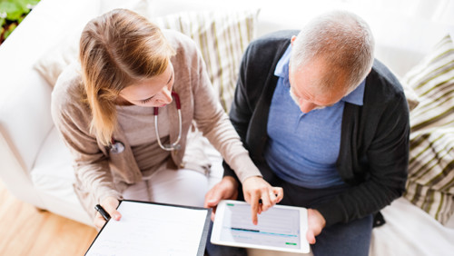 Meneer krijgt hulp van een mevrouw met pgb aanvragen op tablet Meneer krijgt hulp van een mevrouw met pgb aanvragen op tablet