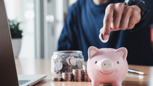 Een spaarpot waar een hand een muntje in gooit Een spaarpot waar een hand een muntje in gooit