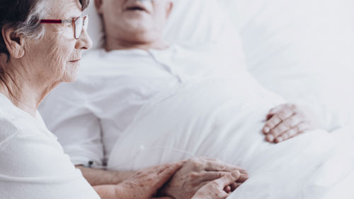 Vrouwelijke mantelzorger zit naast zieke man die in bed ligt in de laatste fase Vrouwelijke mantelzorger zit naast zieke man die in bed ligt in de laatste fase