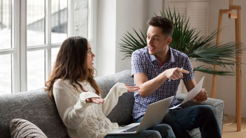 Man met papier en vrouw met laptop op de bank in overleg Man met papier en vrouw met laptop op de bank in overleg