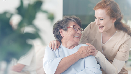 Jonge vrouw en vrouw in rolstoel lachen naar elkaar en houden elkaars hand vast Jonge vrouw en vrouw in rolstoel lachen naar elkaar en houden elkaars hand vast