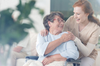 Jonge vrouw en vrouw in rolstoel lachen naar elkaar en houden elkaars hand vast Jonge vrouw en vrouw in rolstoel lachen naar elkaar en houden elkaars hand vast