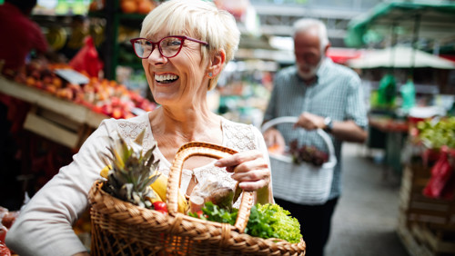 Lachende vrouw op de markt met mand vol gezond eten Lachende vrouw op de markt met mand vol gezond eten