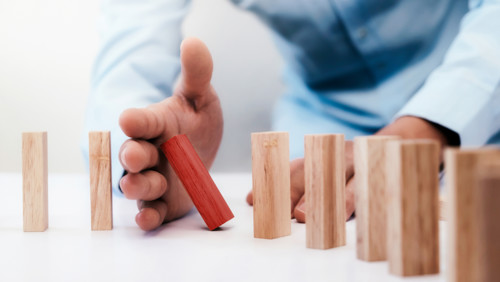 Man steekt hand tussen rode dominosteen dat omvalt Man steekt hand tussen rode dominosteen dat omvalt