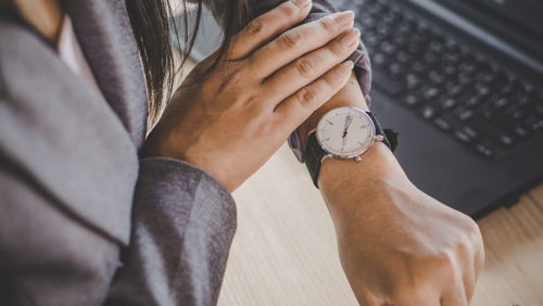 Vrouw zit aan bureau en kijkt op horloge Vrouw zit aan bureau en kijkt op horloge