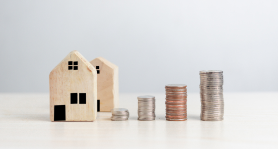 Twee Houten huisjes met daarnaast stapeltjes munten