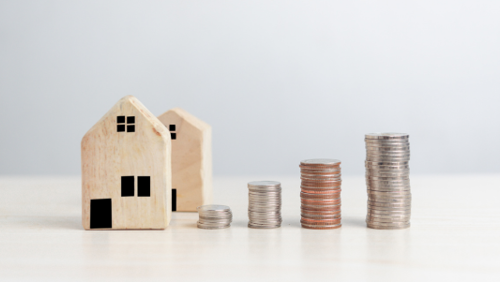 Twee Houten huisjes met daarnaast stapeltjes munten Twee Houten huisjes met daarnaast stapeltjes munten